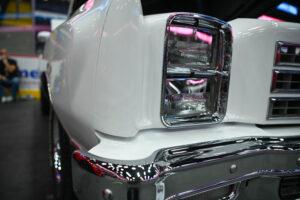 Close-up of a vintage white car's headlight and chrome bumper.