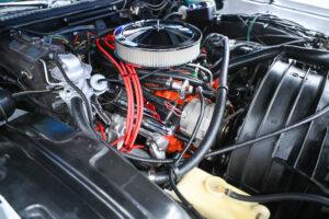 Classic car engine with bright red ignition wires and chrome air filter.