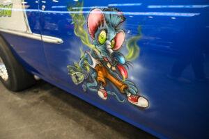 Cartoonish, vibrant graffiti of a crazed character on a blue wall.