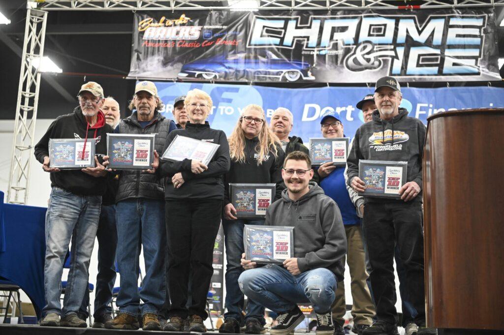 Group of people holding awards at an outdoor event stage.
