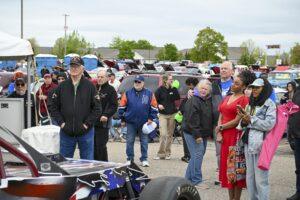 Crowd gathered around a vintage race car at an outdoor event.