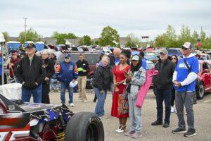Crowd watching a race car at an outdoor event on a cloudy day.