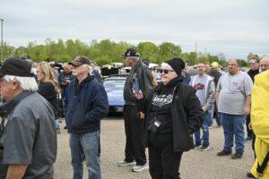 Group of people standing outdoors near cars, dressed for cool weather.