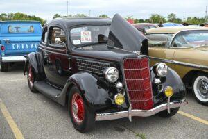 A classic black vintage car with red rims displayed at a car show.