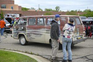 Two people talking near an old, damaged car on a street corner.