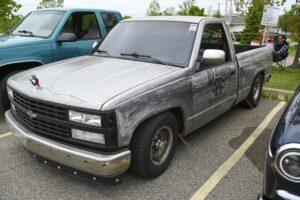 A silver pickup truck parked in a lot with a blue truck nearby.