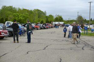 A car show with people walking among vintage cars on a cloudy day.