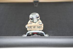 A small pigeon figurine holding a sign that says 'EAT MY DUST'.