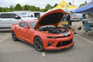 Bright orange sports car with hood open at outdoor event.