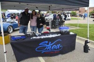 Three people posing behind a Shea branded table at an outdoor event.