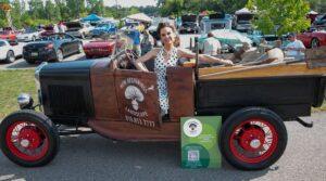 Woman posing with a vintage car at an outdoor event.
