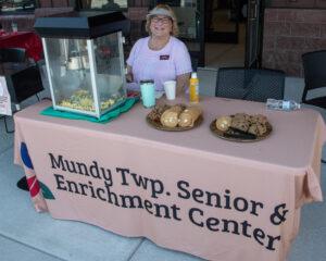 A woman sells popcorn and cookies at a senior enrichment center table.