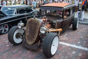 Vintage hot rod car with exposed engine and wide whitewall tires.