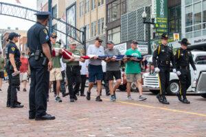 People carry a folded American flag during a ceremony while police officers stand guard.