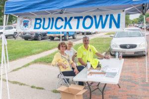 Three people at a Buicktown booth outdoors under a blue canopy.