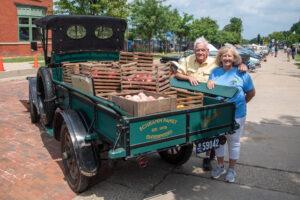 Two women standing beside a vintage green truck loaded with pigs.
