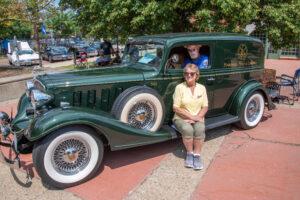 Two people posing with a vintage green car outdoors on a sunny day.