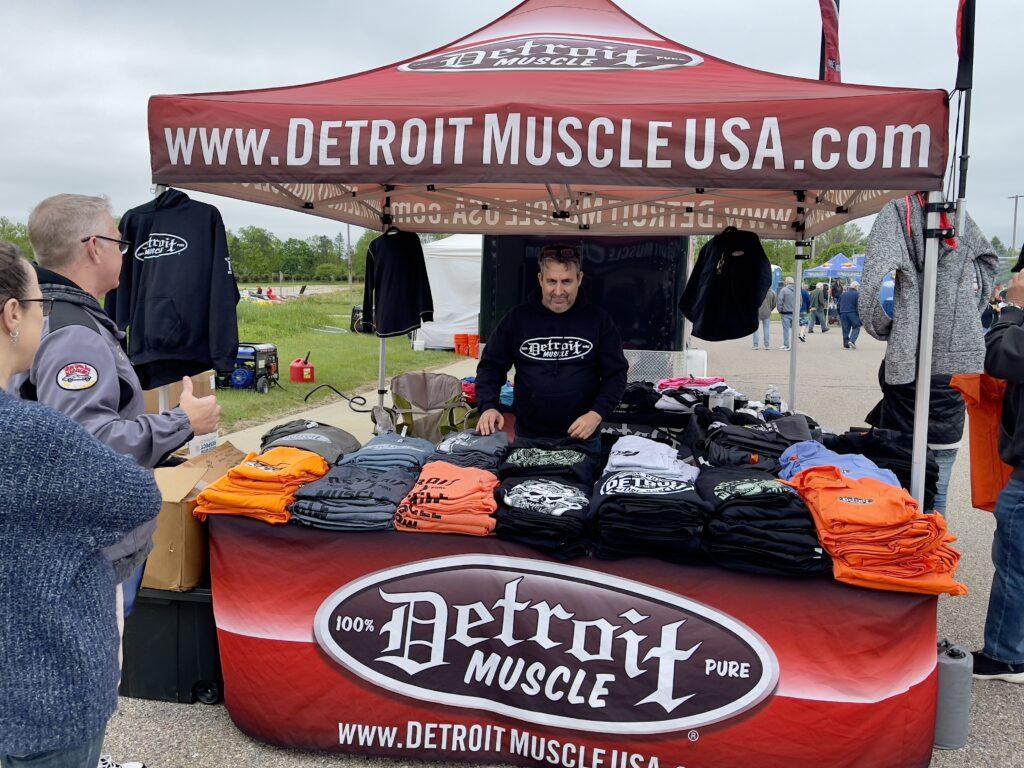 Man selling shirts at outdoor booth.