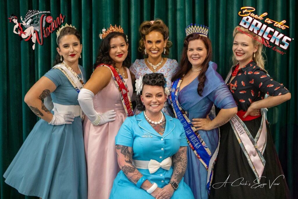 Women in vintage dresses with crowns smiling.