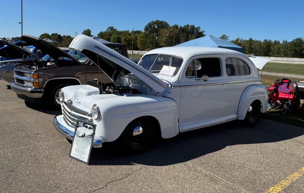 White vintage car with hood open, displayed.