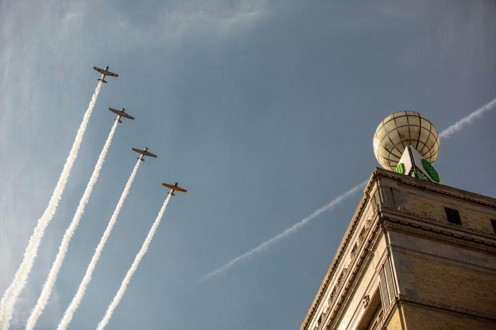 Planes flying in formation near building tower.