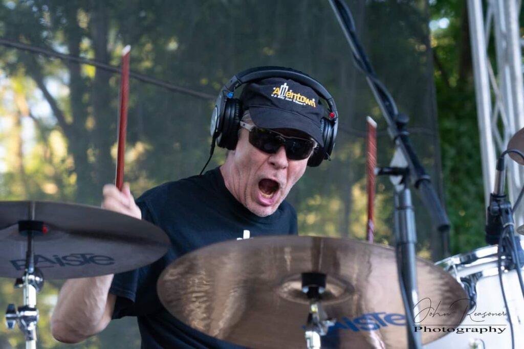 Drummer passionately playing drums outdoors.