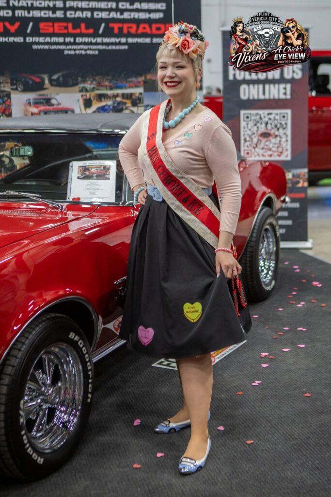Woman in vintage attire poses by classic car.